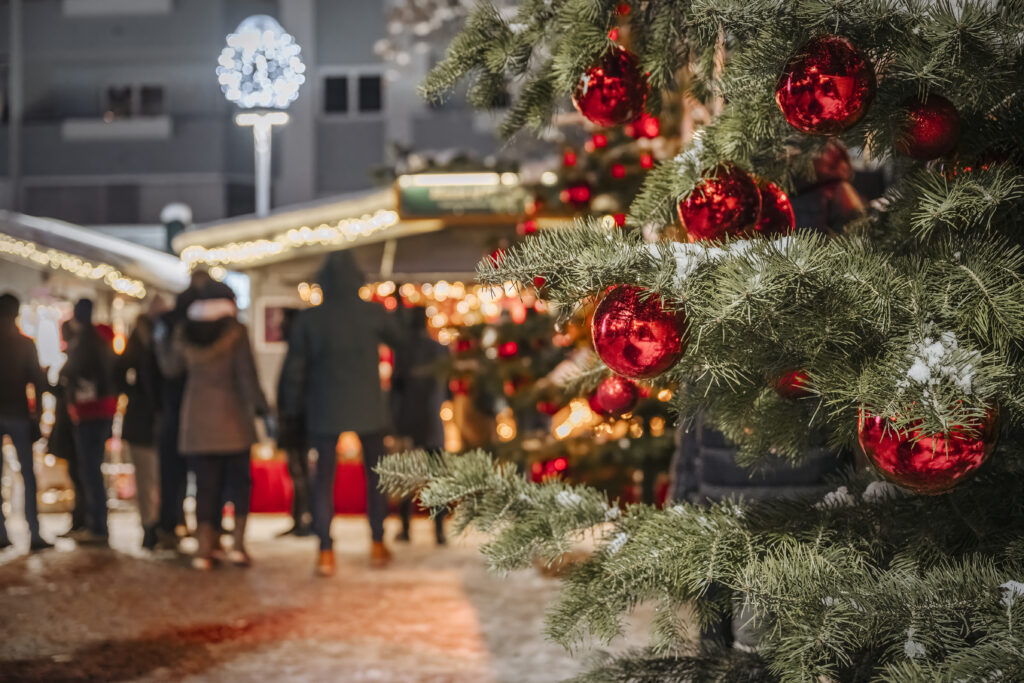 Decorazioni natalizie rosse su un albero di Natale con bancarelle illuminate e persone sullo sfondo al mercatino di Natale di Kufstein.