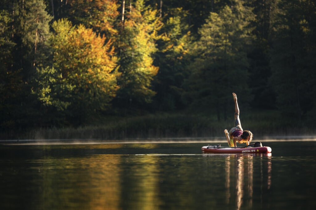 Persona pratica yoga su una tavola SUP sul lago Hechtsee, circondata da alberi autunnali