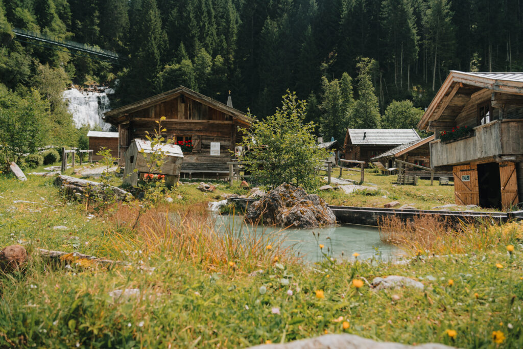Tradition erleben im Mühlendorf Gschnitz: Zwischen alten Holzhäusern, Wasserläufen und Blick auf den Sandeswasserfall entdecken Familien das bäuerliche Leben vergangener Zeiten – anschaulich, naturnah und ideal für einen erlebnisreichen Ausflug.
