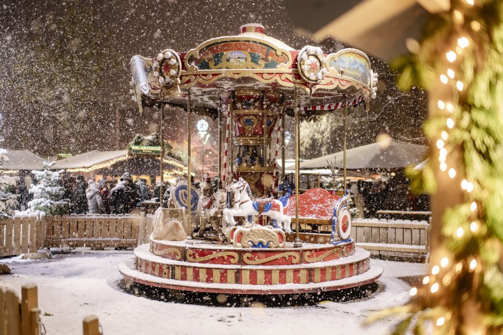 Giostra natalizia con cavalli a dondolo al mercatino di Natale a Kufstein, innevata e illuminata