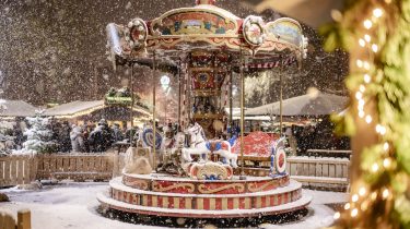 Giostra natalizia con cavalli a dondolo al mercatino di Natale a Kufstein, innevata e illuminata
