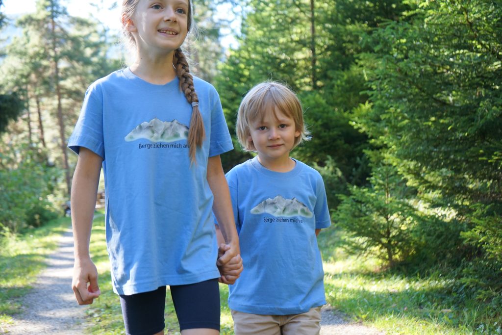 Ganz neu im Sortiment – die Kinder-T-Shirts mit dem Aufdruck „Berge ziehen mich an“ zeigen schon bei den Kleinsten die Verbundenheit zu den Bergen.
