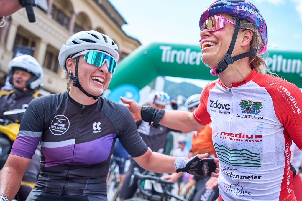 Zwei erschöpfte, lachende Rennradfahrerinnen in Sportkleidung gratulieren sich nach einem Rennen im Zielbereich.