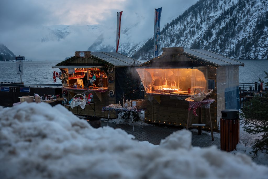 An der Schiffsanlegestelle Scholastika in Achenkirch am Achensee locken hell erleuchtete Marktstände mit Kunsthandwerk zur Landweihnacht.